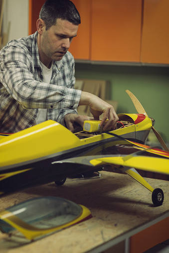 Mid adult man assembling parts of airplane in his workshop.