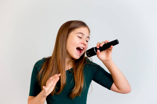 niña cantando con un micrófono - cantar fotografías e imágenes de stock