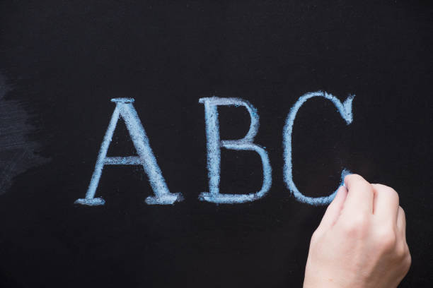 istock Female hand writing alphabet on black chalkboard. Educational background with ABC letters with copy space 923361050