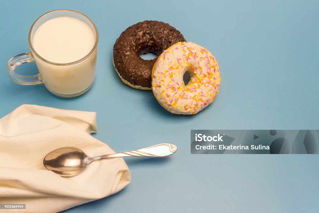 Glasierte Donuts, Milch in eine Glasschale, ein kleiner Löffel und eine Serviette auf blauem Hintergrund - Lizenzfrei Blau Stock-Foto