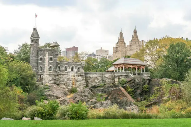 Belvedere Castle in Autumn, Central Park. It contains exhibit rooms and an observation deck. Since 1919, the castle has also been the location of the official Central Park weather. Trees in Autumn Colors (Foliage), Rocks, Landscaped grass, American flag and Overcast Sky are in the image. HDR image.