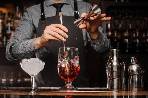 barman faisant une boisson alcoolisée avec de la glace dans un verre à cocktail - cocktail alcohol red martini glass photos et images de collection