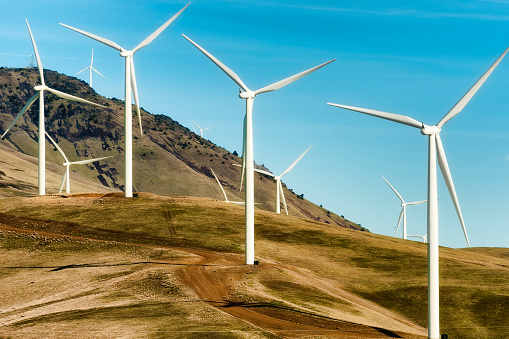 Windturbines stand tall and stark against the high desert landscape of rolling hills in the Columbia River Gorge