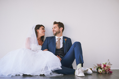 Studio shot of a newly married young couple sitting together on the floor against a gray background