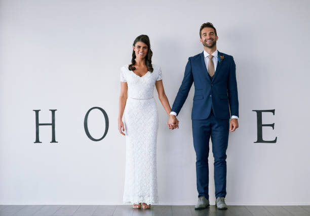 Concept studio shot of a bride and groom making an M in the word “home” against a wall