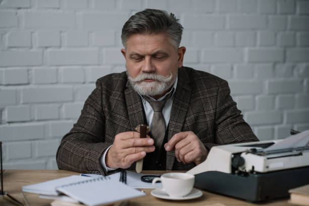 istock senior writer looking at watch while sitting at workplace 923391532