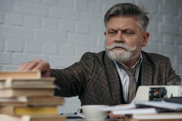 istock close-up shot of bearded senior writer at workplace taking book from stack 923401420