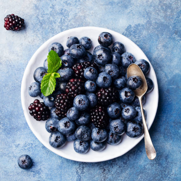 istock Blueberry and blackberry berries on a white plate on blue stone background. Top view 923404068