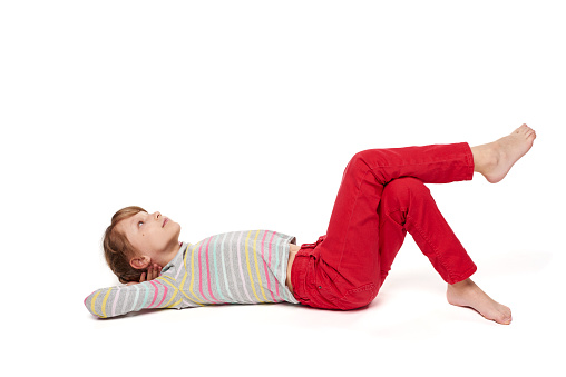 A child girl lying on her back on the floor with crossed legs looking up at blank copy space, over white background