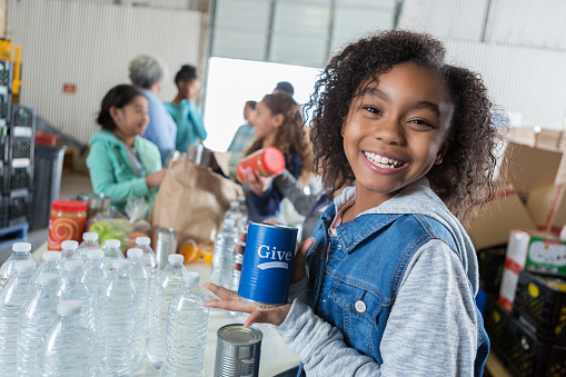 Beautiful young girl smiles while holding a can to collect money during a food drive in her community.