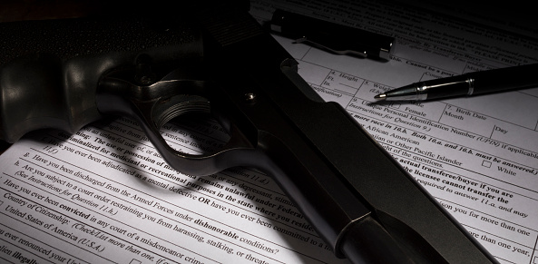Gun and pen on firearm purchase paperwork with dishonorable discharge question highlighted