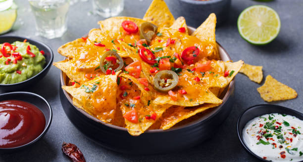 Nachos chips with melted cheese and dips variety in black bowl. Grey stone background Nachos chips with melted cheese and dips variety in black bowl. Grey stone background. nacho chip photos stock pictures, royalty-free photos & images
