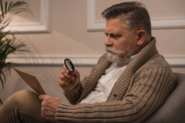 istock senior man reading letter with magnifying glass while sitting in armchair 923433882