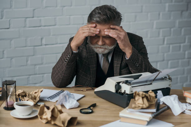 istock depressed senior writer sitting at his messy workplace and holding head with hands 923434582