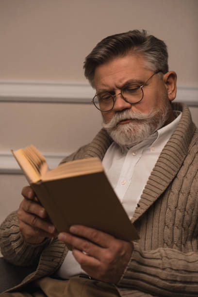istock concentrated senior man in eyeglasses reading book 923434718