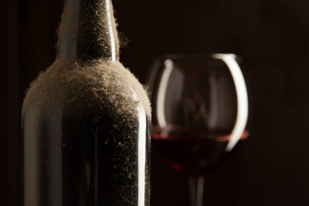 Dusty vintage wine bottle and wineglass with red wine over dark background