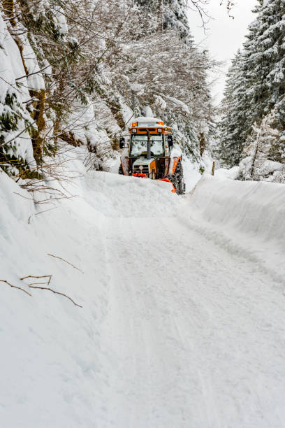 In Ljosland, Norway, it's a gray day. February 4, 2013 a lot of snow has fallen. The tractor clears the road from snow during the bad weather. It is a foggy day. This means there is little visibility. The shovel loading platform is raised. Behind the shovel, the machine scrapes the snow from the street and sprays the snow from the roadside jug into the roadside.