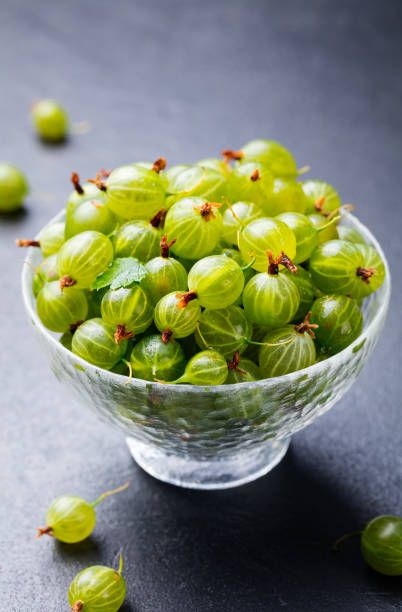istock Gooseberries in glass bowl on black stone slate background. 923438628