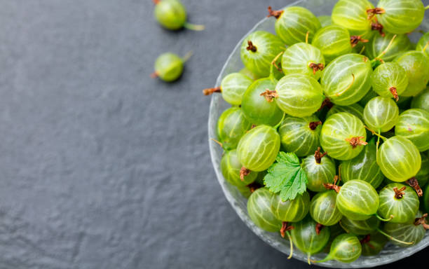 istock Gooseberries in glass bowl on black stone slate background. Top view. Copy space. 923438822