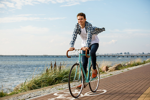 Smiling young businessman with a bag wearing a cycling helmet and walking with his bike after leaving work