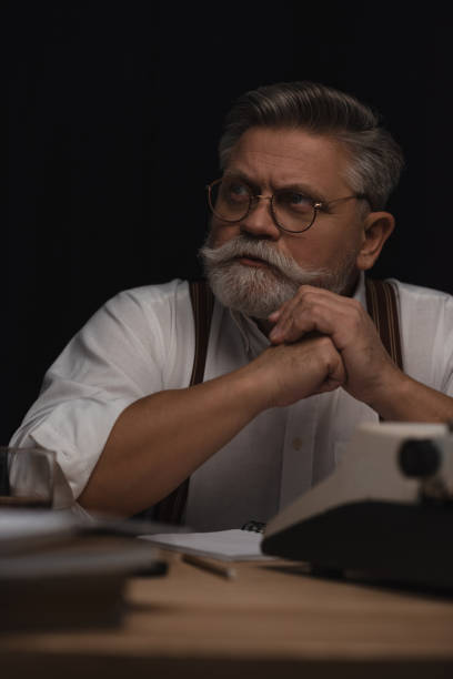 istock thoughtful senior writer sitting at workplace and looking away isolated on black 923441276