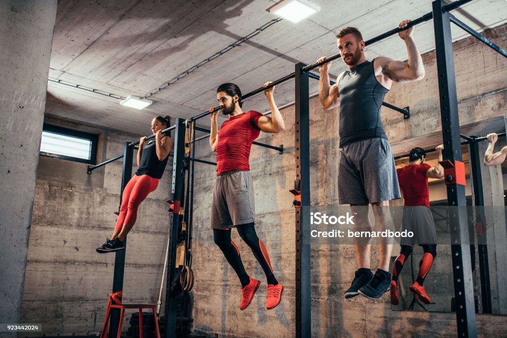 Set a goal and make it happen Shot of two young men and a woman doing pull ups Chin-Ups Stock Photo