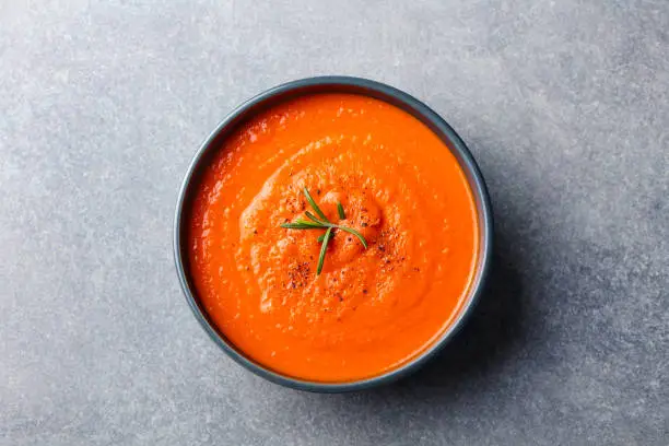 Tomato soup in a black bowl on grey stone background. Top view. Copy space.