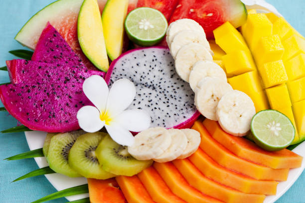 istock Tropical fruits assortment on a white plate with palm leaf. Blue background. Top view. Copy space 923447872