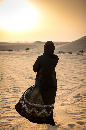Woman in a burka Burqa walking over a middle eastern desert during sunset.