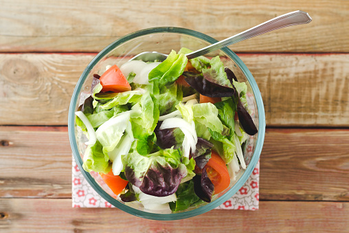 Salad in glass bowl over wooden background. Top view.