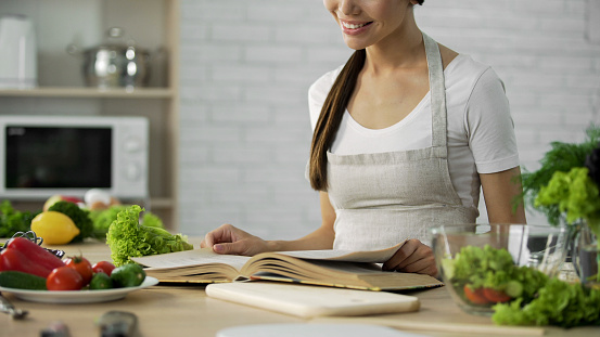 Asian female reading ingredients list for salad in cooking book at home kitchen, stock footage
