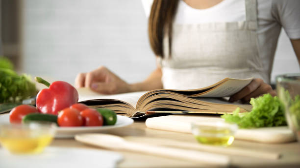 Housewife reading cooking book with fresh vegetables and kitchen tools on table Housewife reading cooking book with fresh vegetables and kitchen tools on table, stock footage recipe stock pictures, royalty-free photos & images