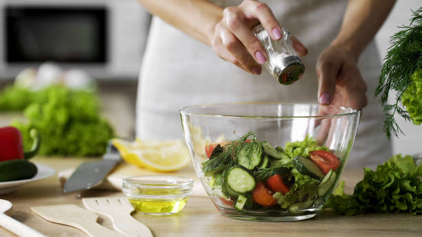 野菜サラダのガラスのボウル、ヘルスケア、過剰な塩を追加する女性の塩漬け - 塩をふる ストックフォトと画像
