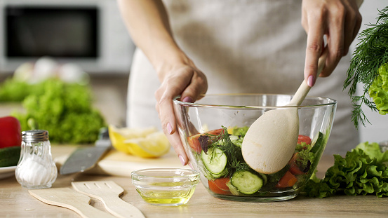 Mother mixing salad in glass bowl by big wooden spoon, traditional family recipe, stock footage