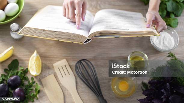 Lady Reading Pizza Recipe In Culinary Book At Home With Kitchenware On Table Stock Photo - Download Image Now