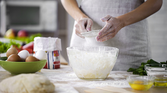 Woman hands sieving flour over glass bowl with dough, adding baking ingredients, stock footage