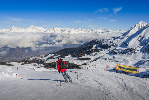 Pila, Aosta, Italy - Feb 19, 2018: One skier in jeans going downhill a piste with panoramic view of wide and groomed ski piste. View Towards north is Switzerland and its iconic Matterhorn