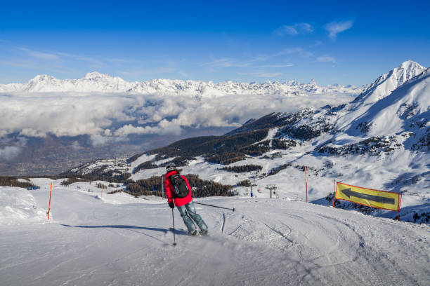One skier in jeans going downhill a piste with panoramic view of wide and groomed ski piste. View Towards north is Switzerland and its iconic Matterhorn Pila, Aosta, Italy - Feb 19, 2018: One skier in jeans going downhill a piste with panoramic view of wide and groomed ski piste. View Towards north is Switzerland and its iconic Matterhorn pila stock pictures, royalty-free photos & images