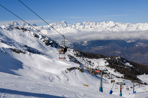 Pila, Aosta, Italy - Feb 19, 2018: Chairlift at Italian ski area of Pila on snow covered Alps and pine trees during the winter with Mt. Blanc in France visible in background
