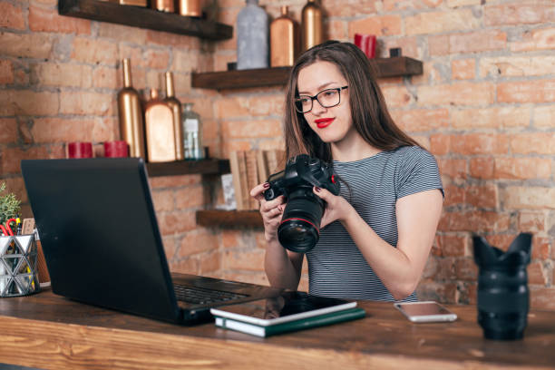 istock Young freelancer girl is working with notebook and photo camera in loft interior 923498328