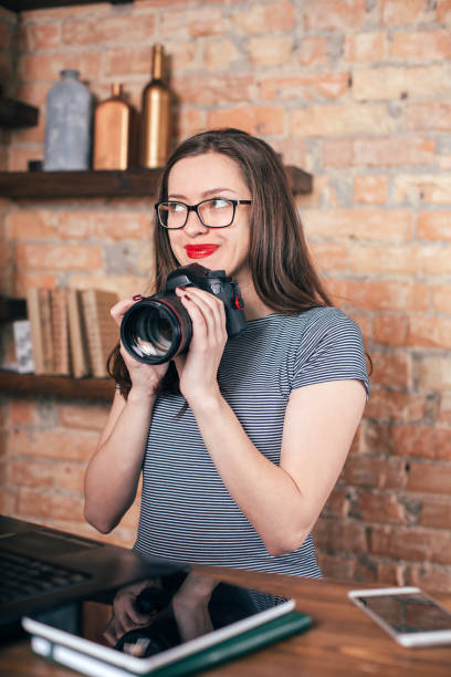istock Young freelancer girl is working with notebook and photo camera in loft interior 923498356
