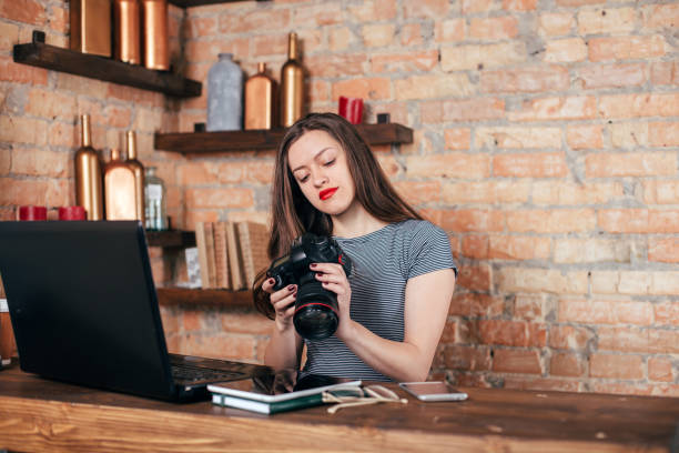 istock Young freelancer girl is working with notebook and photo camera in loft interior 923498382