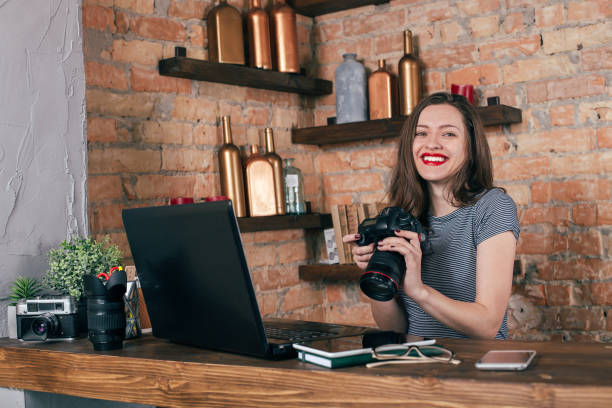 istock Young freelancer girl is working with notebook and photo camera in loft interior 923498428