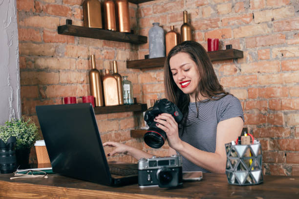 istock Young freelancer girl is working with notebook and photo camera in loft interior 923498436