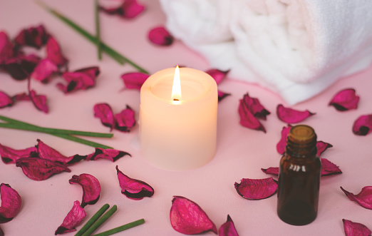 Scented candle and dry petals on pink background; wellness or spa background