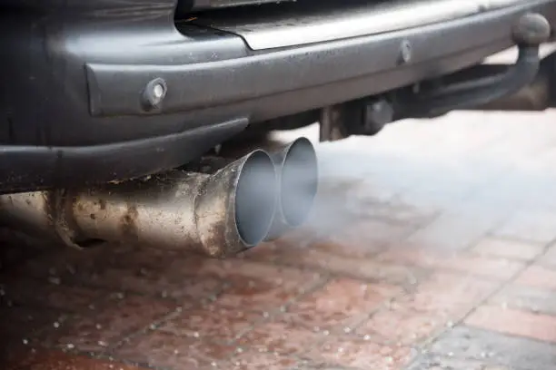 Double exhaust from an older car with diesel engine blows out gas with high particulate matter pollution, copy space, selected focus