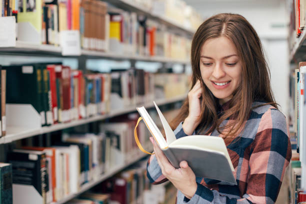 istock Young female girl  student smiling with book in library 923511944