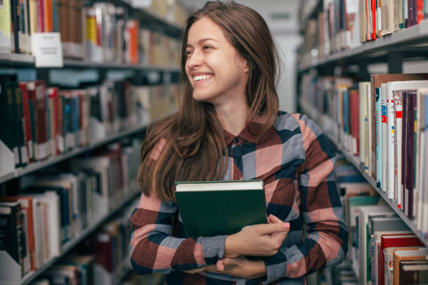 istock Young female girl  student smiling with book in library 923512002