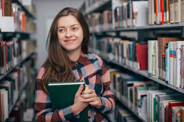 istock Young female girl  student smiling with book in library 923512016