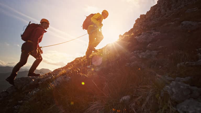 Rope team of two mountaineers climbing the mountain in setting sun